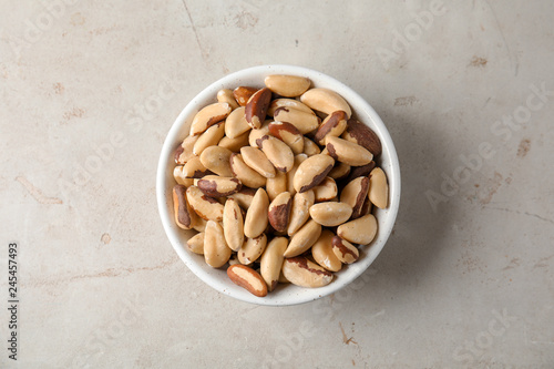 Bowl with tasty Brazil nuts on grey background, top view