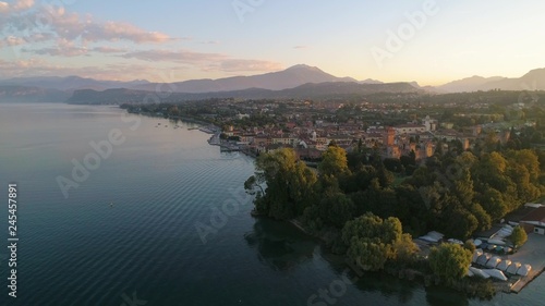 Italian castle, C4k aerial, reverse, drone shot, of Lazise fortress and the east coast of lago di Garda, on a sunny, summer morning dawn, in Verona, Italy