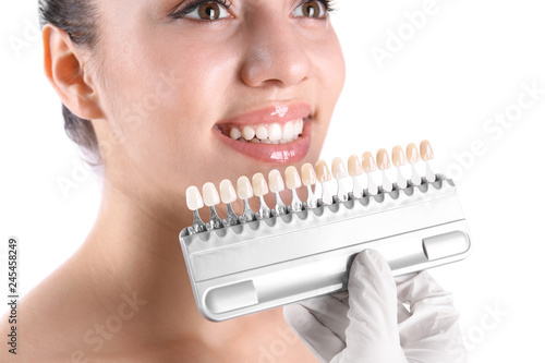 Dentist checking young woman's teeth color on white background, closeup
