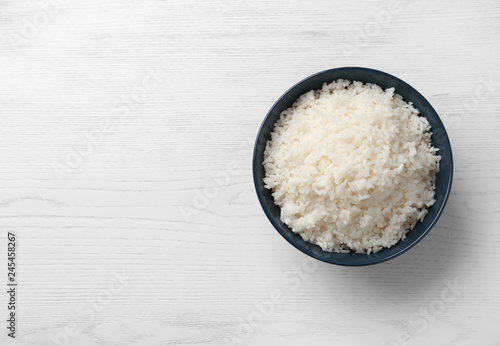 Bowl of boiled rice on wooden background, top view with space for text