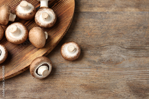 Fresh champignon mushrooms and cutting board on wooden table, top view with space for text