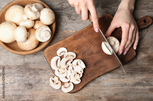 Young woman cutting fresh champignon mushrooms on wooden board, top view