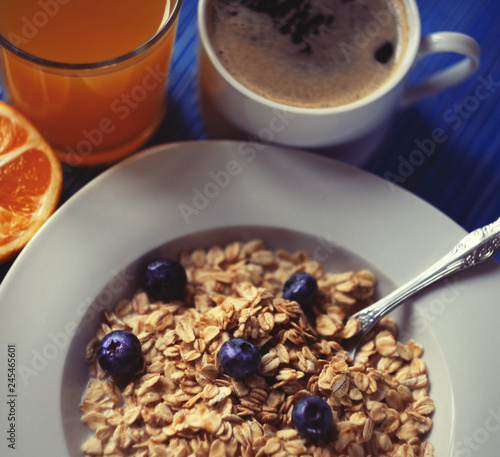 Oatmeal porridge with fresh blueberries, almonds, coffee and orange juice in white bowl on blue table.