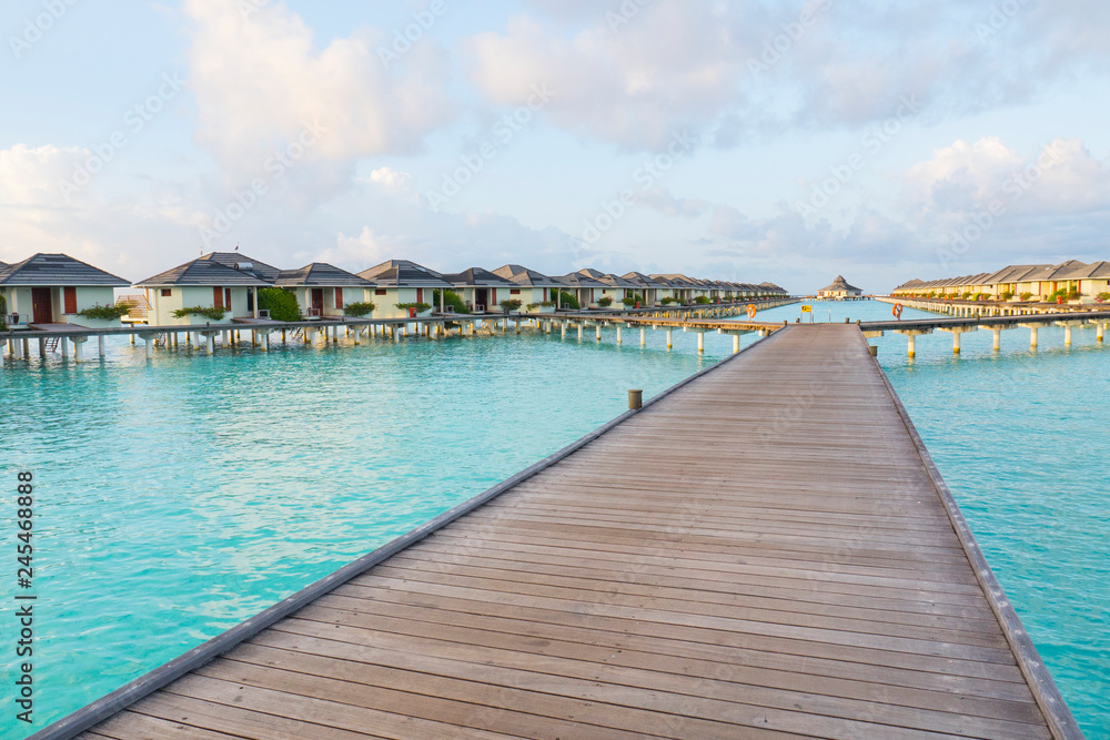 Water Bungalows at Tropical beach in the Maldives at summer day. Sea and the resort like paradise relax concept. Long wodden jetty extended into azure water of lagoon with villas over the ocean.