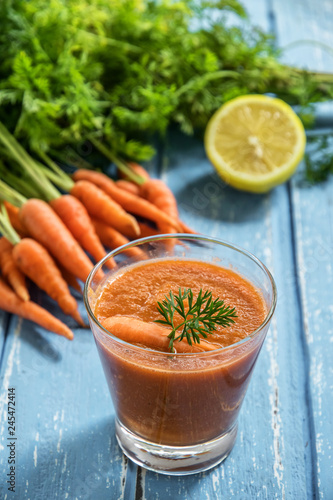 Fresh carrot smoothie in glass on rustic wooden background.