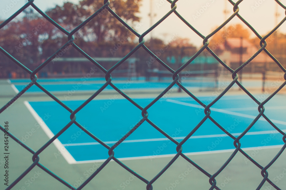Fototapeta premium Close up metal fence with empty outdoor blue tennis hard court in the background. (Selective focus)