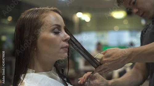 Beautiful brunette woman receiving haircut with scissors in beauty studio. Hairstylist cutting female hair in hairdressing salon. Female hairstyle. Beauty industry.