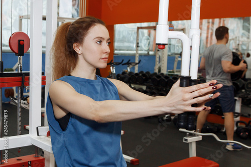 Young pretty woman doing physical exercises on a simulator in the gym.
