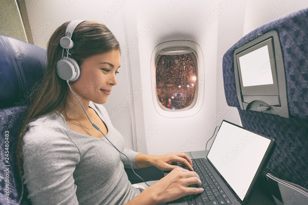 Fototapeta premium Samolot pasażerski biznes kobieta profesjonalna praca w kabinie samolotu podczas lotu z wifi w czasie pisania pisania na komputerze typu tablet słuchanie muzyki w słuchawkach. Młody podróżnik azjatycki.