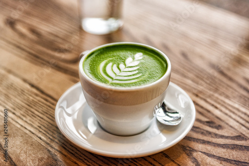 Matcha latte green milk foam cup on wood table at cafe. Trendy powered tea trend from Japan.