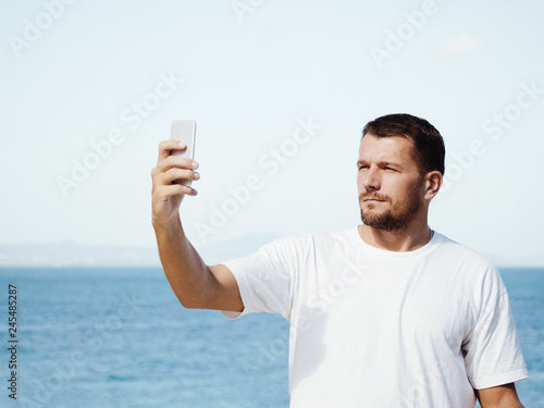 A man on vacation makes a selfie on a smartphone. Sunny day, ocean background.