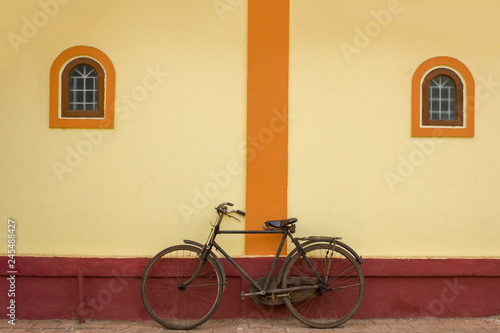 black rusty old bicycle stands on a beige wall with two windows
