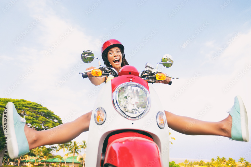 Naklejka premium Zabawa w podróży, zabawny turysta, beztroska jazda skuterem na letnią podróż. Krzycząca Azjatycka dziewczyna wygłupia się z nogami na motocyklu.