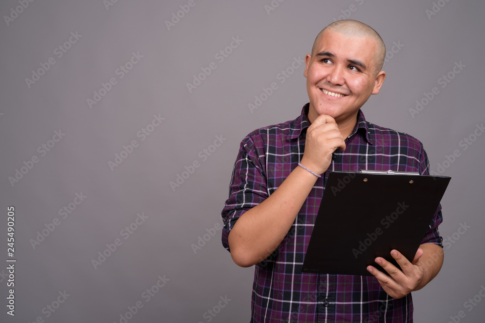 Young bald Asian businessman against gray background Young bald Asian businessman against gray background