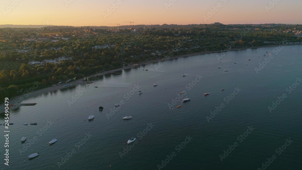 Motorboats on a lake, C4k aerial, drone shot, of  covered boats, anchored at the coast of lago di Garda, on a sunny, summer morning dawn, in Veron, Italy