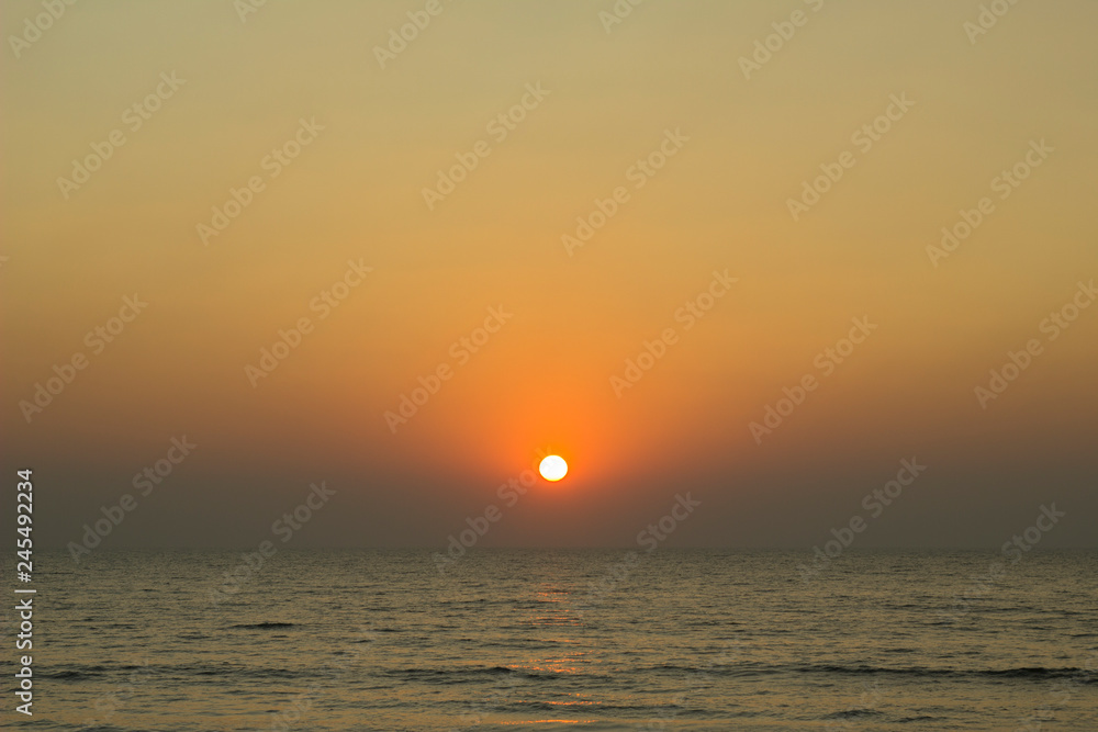 bright sun over the horizon in a purple pink gray evening sky against the background of the ocean