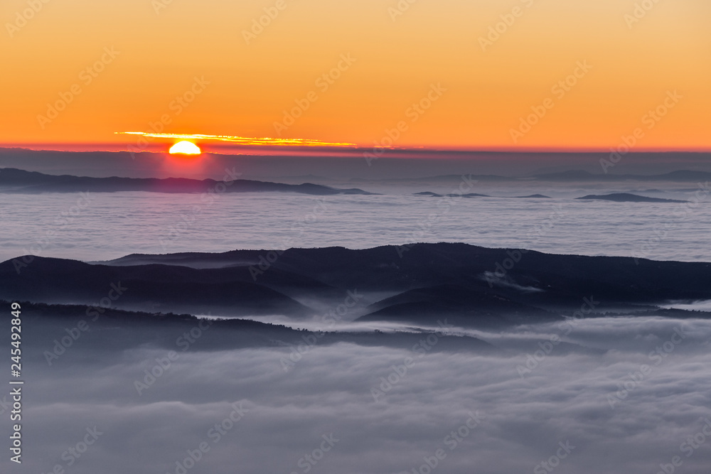 Obraz premium Beautiful sunset over a valley filled by fog with mountains and hills