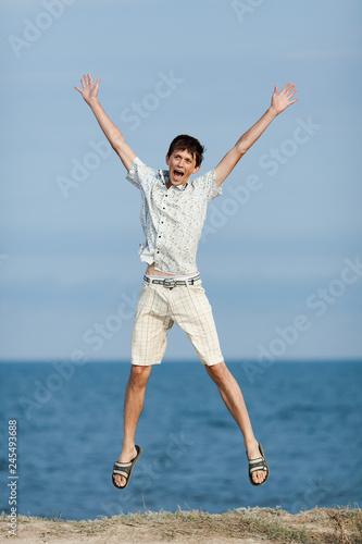 Young man jumping with hands raised against sea