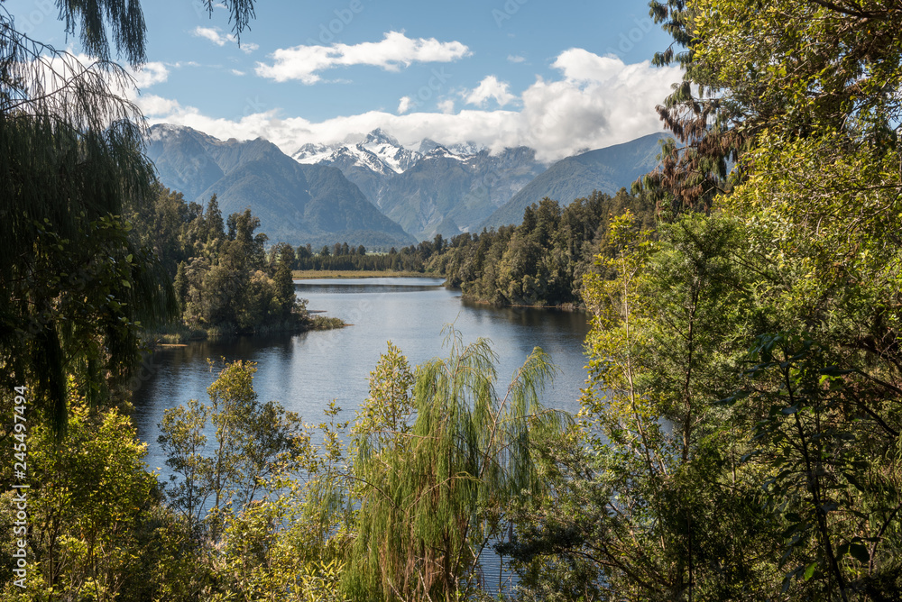 Lake Matheson on the West Coast of New Zealand surrounded by forest, with Mounts Cook and Tasman of the Southern Alps in the background.