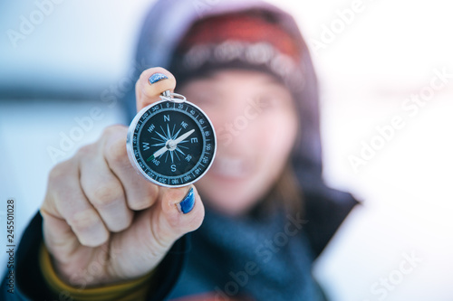 Young woman with gloves is holding up a compass, outside in the winter photo