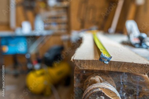 Tape measurer on long oak board in a small wood workshop, shallow depth of field.