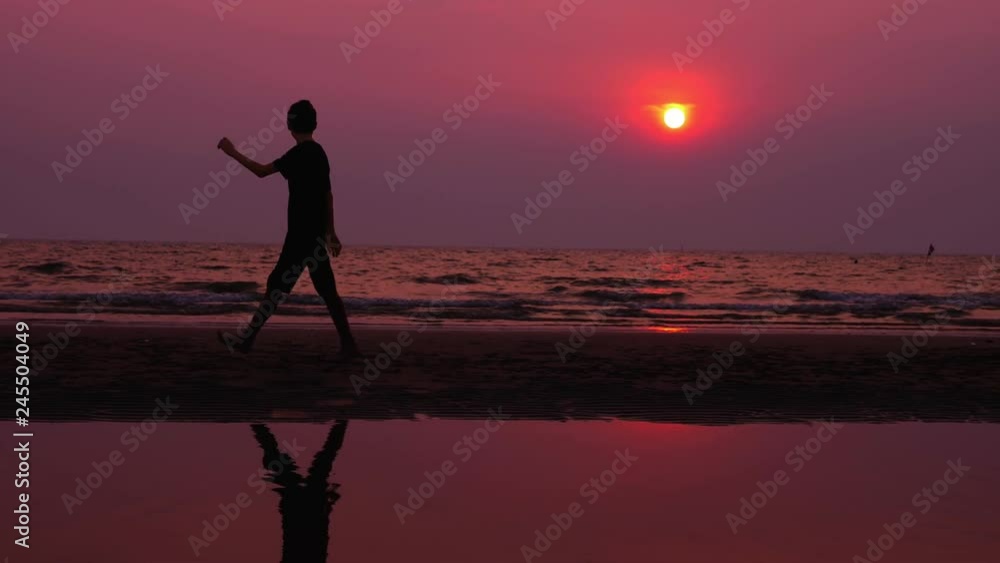 silhouette. lonely asian young man walking peacefully along a deserted beach at sunset. seascape silhouette. lonely asian young man walking peacefully along a deserted beach at sunset. seascape