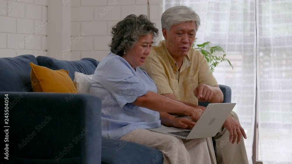 Asian senior couple using laptop searching online shopping. Sharing social media communication in living room at home. Slow motion movement. Asian senior couple using laptop searching online shopping. Sharing social media communication in living room at home. Slow motion movement.