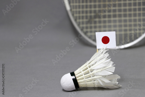 Mini Japan flag stick on the white shuttlecock on the grey background and out focus badminton racket. photo