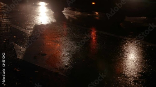 Night city street after rain, low angle view, car light reflections on wet road