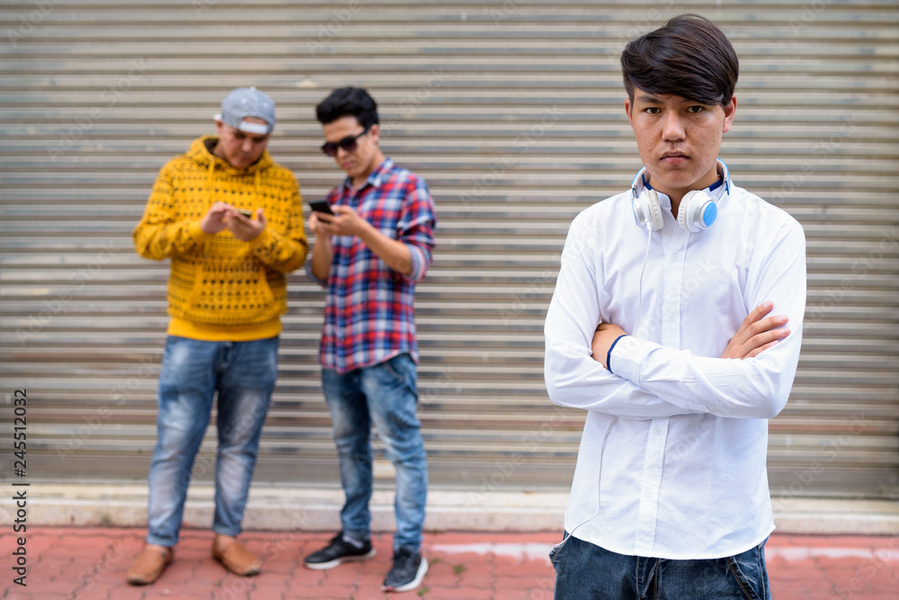 Three young Asian men standing against warehouse door in the str