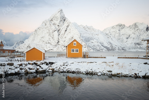 Yellow fishing rorbuer builded from wood on the white snow of winter with mountain view on the background in Reine village at Lofoten Norway