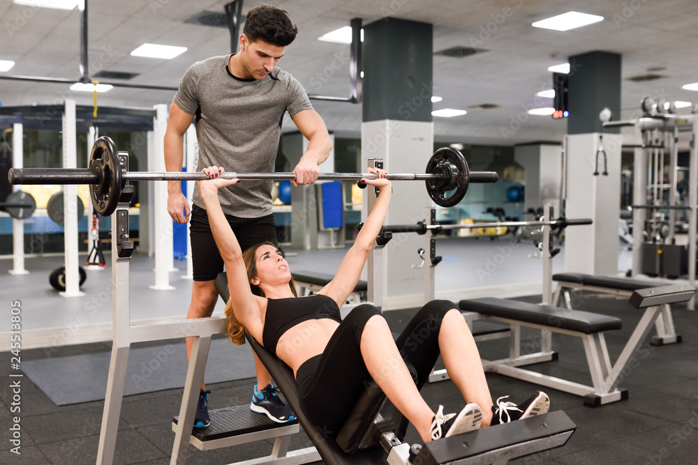 Fototapeta premium Personal trainer helping a young woman lift weights