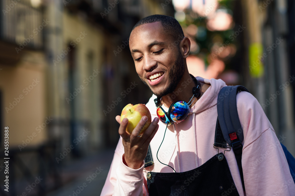 Young black man eating an apple walking down the street. Stock Photo ...