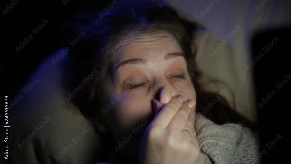 beautiful sleepy woman lying on the couch in a dark room late at night with smartphone in hand beautiful sleepy woman lying on the couch in a dark room late at night with smartphone in hand