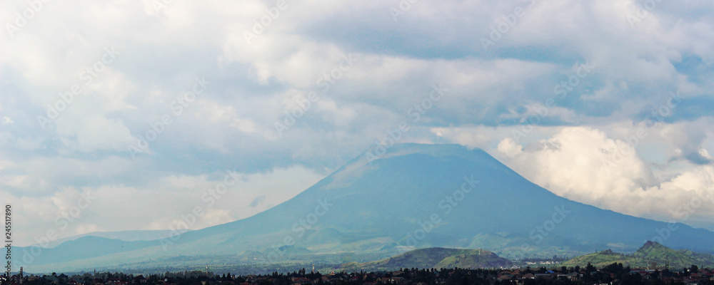 Distant view of Mount Nyiragongo, located in Virunga National Park, in the Democratic Republic of Congo (DRC). It is an active volcano with a lava lake. Mountain peak - landscape with clouds.