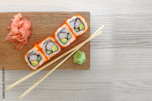 Sushi rolls with chopsticks on a wooden platter, with wasabi and pickled ginger; Maki sushi isolated on a grey wood background photo