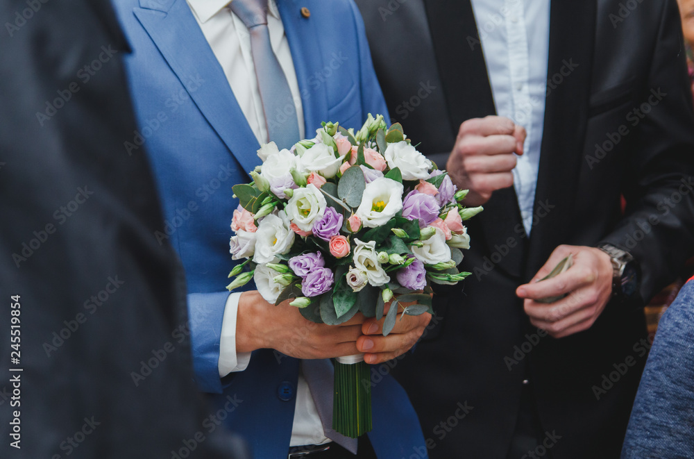 Groom in blue suit is holding beautiful elegant wedding bouquet in hands. Eustoma, freesia and pink roses flowers. Groom in blue suit is holding beautiful elegant wedding bouquet in hands. Eustoma, freesia and pink roses flowers.