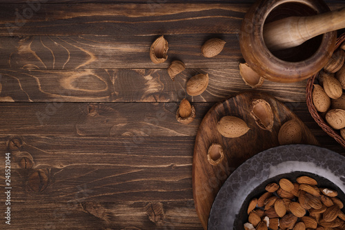 Flat lay of almonds in black plate with other accessories on brown wooden background top view
