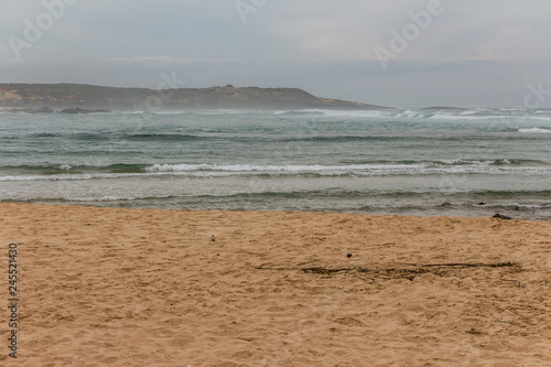 Empty sandy beach. View over the open ocean. Wavy ocean. Cloudy day. Nature scenery.