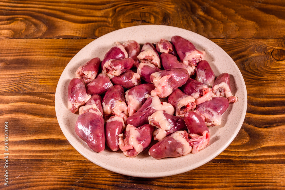 Ceramic plate with raw chicken hearts on wooden table