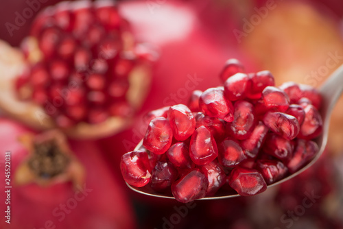 Spoon with pomegranate seeds on fresh ripe pomegranates background 3