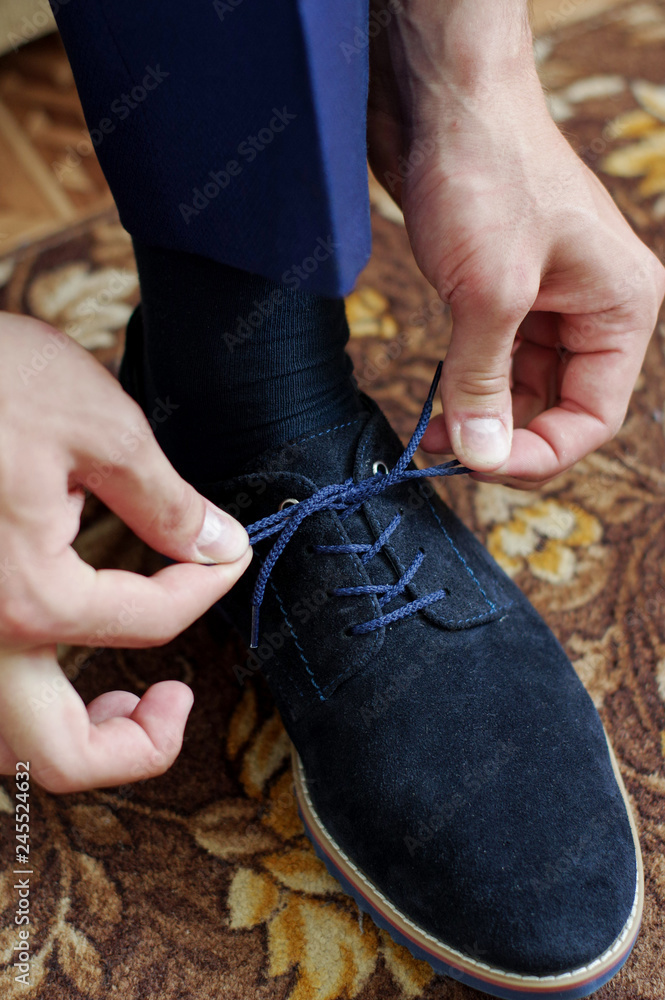 The man ties the shoelaces on the shoes. Business formal style of clothing. Official event. Wedding. Morning of the groom. Cropped image
