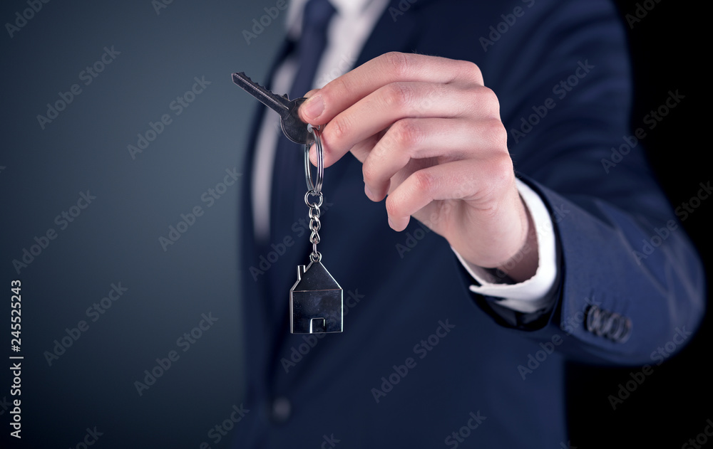 Young businessman hand over keys with empty dark background
Young businessman hand over keys with empty dark background