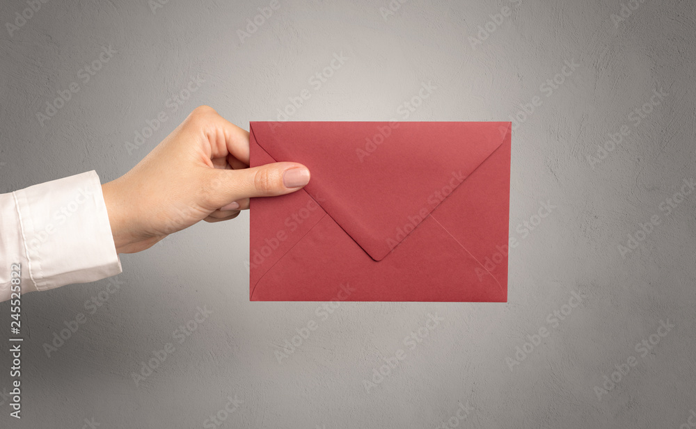 Female hand holding coloured and white envelope with empty wall background
