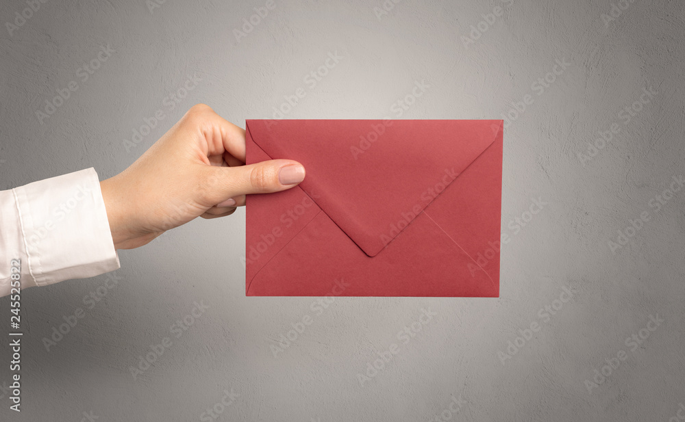Fototapeta premium Female hand holding coloured and white envelope with empty wall background 