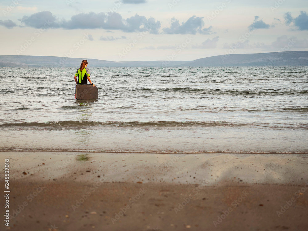 Girl in wetsuit going into water with her small serf board. Mountains in the background, calm water. Concept outdoor activities, active live style. Girl in wetsuit going into water with her small serf board. Mountains in the background, calm water. Concept outdoor activities, active live style.