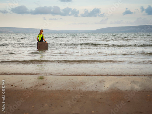 Girl in wetsuit going into water with her small serf board. Mountains in the background, calm water. Concept outdoor activities, active live style.