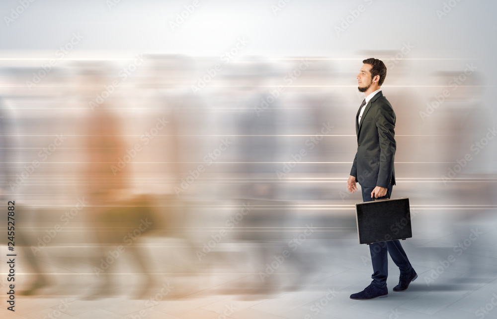 Obraz premium Young businessman with briefcase hurry up on a crowded street with blurred people around 