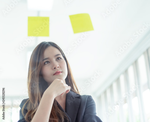 Confident asian business women entrepreneurs young financial assistant business woman working and thinking new ideas on new project with many sticky notes on window at the modern office interior.