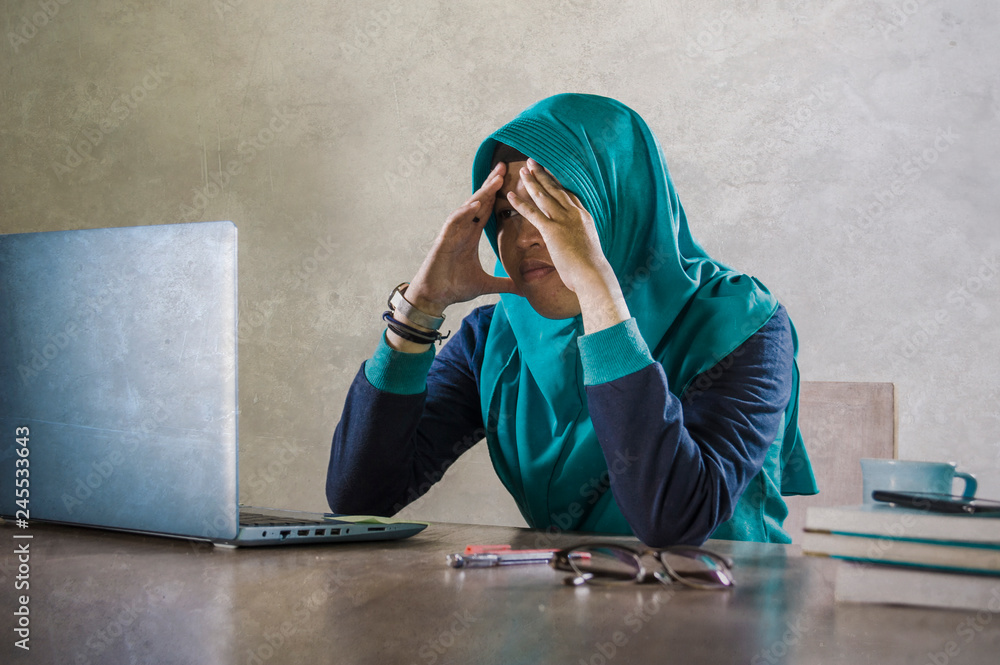young stressed and overwhelmed Muslim student woman in Islam hijab head scarf studying tired feeling overworked working with laptop computer and University books young stressed and overwhelmed Muslim student woman in Islam hijab head scarf studying tired feeling overworked working with laptop computer and University books